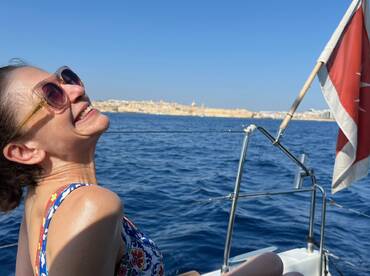 A joyful woman enjoys a sunny day sailing on the ocean, with a picturesque coastal landscape in the background — a perfect moment of relaxation and adventure.