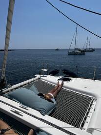A guest relaxes on the netting of a catamaran, enjoying the sun and ocean views — a perfect moment for a tranquil getaway on the water.