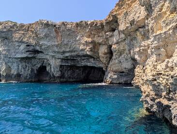 A stunning view of rocky cliffs and a cave along the coastline, showcasing the vibrant blue waters — perfect for exploring natural wonders by boat.
