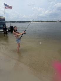 A young girl enjoys a fishing experience in shallow water, showcasing the excitement of catching a fish while having fun outdoors.