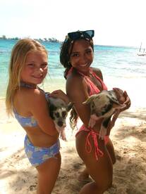 A joyful moment captured with a child and an adult holding adorable pigs on the beach, showcasing a unique wildlife interaction in the Bahamas.