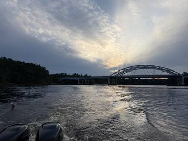 A picturesque view of a bridge at sunset, captured from a boat, showcasing the serene beauty of the waterway and surrounding nature.