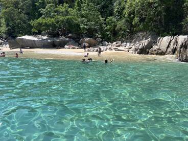 A lively beach scene with people enjoying the clear waters and sandy shore, perfect for a fun day of swimming and relaxation.