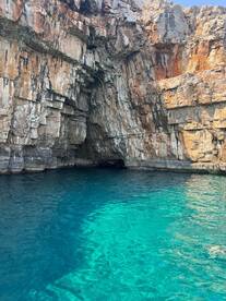 A stunning view of a rocky coastline with a cave entrance, surrounded by crystal-clear turquoise waters — a perfect destination for exploration and adventure.