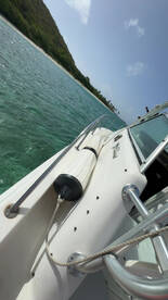 A close-up view of a boat's exterior showcasing its sleek design and features, set against a backdrop of clear turquoise waters and lush greenery.