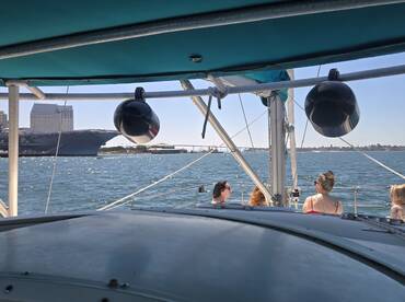 A group of friends enjoys a sunny day on a sailboat, with a stunning cityscape in the background — perfect for a memorable sailing experience.