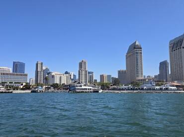 A stunning view of the San Diego skyline from the water, showcasing the vibrant cityscape against a clear blue sky — perfect for sightseeing and exploring the waterfront.