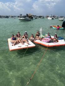 A lively group of friends enjoys a day on the water, relaxing on floating mats and soaking up the sun — the perfect summer party atmosphere.