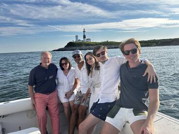 A cheerful group poses together on a boat with a picturesque lighthouse in the background, capturing a memorable moment on the water.