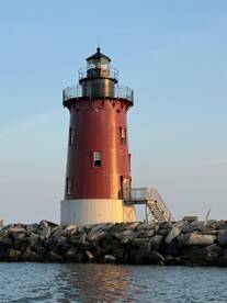 A striking red lighthouse stands tall against a clear sky, marking the entrance to a harbor. Its unique design and coastal setting make it a picturesque landmark.
