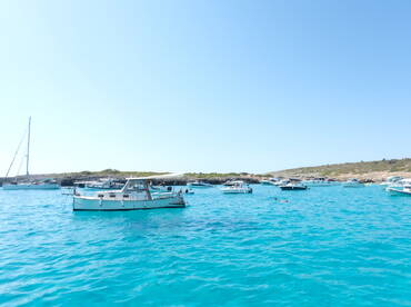 A vibrant scene of boats anchored in crystal-clear turquoise waters, with people enjoying the sun and swimming — a perfect summer getaway.