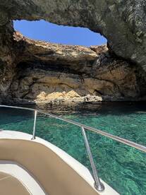 A stunning view of a natural cave with crystal-clear waters, where a group enjoys swimming — a perfect highlight of a boating adventure.