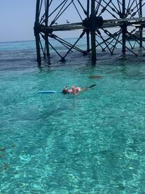 A child enjoys snorkeling in crystal-clear waters beneath a pier, showcasing the beauty of underwater adventures.