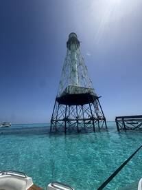A stunning view of a lighthouse standing tall above the crystal-clear waters, with boats and snorkelers enjoying the vibrant surroundings — a perfect spot for sightseeing and aquatic adventures.