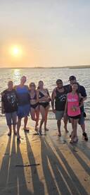 A cheerful group poses together on the beach at sunset, capturing a memorable moment of celebration and camaraderie by the water.