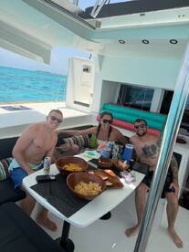 A cheerful group enjoys snacks and drinks aboard a boat, surrounded by stunning turquoise waters — perfect for a fun day on the water.