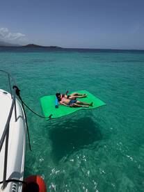 A couple relaxes on a floating mat in the stunning turquoise waters, enjoying a perfect day under the sun — an ideal scene for summer getaways.