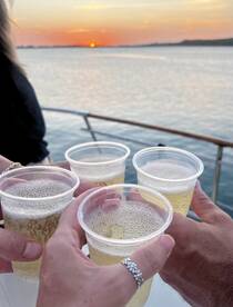 A group toasts with drinks against a stunning sunset backdrop, capturing the essence of celebration on the water.
