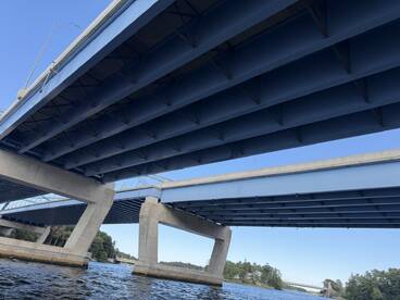 An image depicting the underside of two blue bridges over water, with no identifiable subjects or activities present.