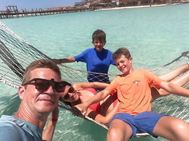 A joyful family enjoys a relaxing moment in a hammock over clear turquoise waters, capturing the essence of a perfect beach day.