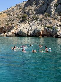 A lively group enjoys a refreshing swim in crystal-clear waters, playing with pool noodles and having fun under the sun — perfect for summer adventures.