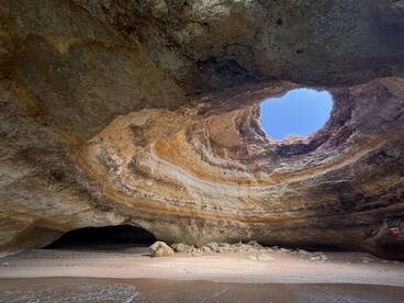 A stunning view of a natural cave with a circular opening, showcasing the beautiful sandy beach below — a perfect spot for exploration and adventure.