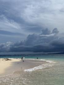 A serene beach scene featuring gentle waves lapping at the shore, with dramatic clouds overhead — a perfect backdrop for a relaxing day by the water.