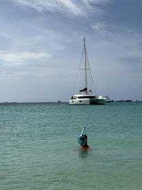 A child enjoys snorkeling in clear waters with a catamaran in the background, capturing the essence of a fun-filled day on the water.