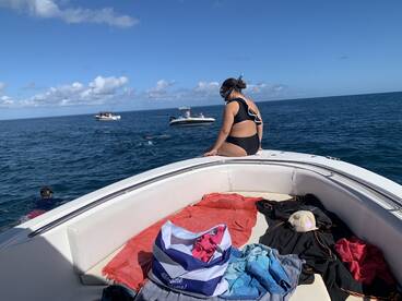 A snorkeler enjoys the ocean while sitting on the edge of a boat, with other boats and swimmers visible in the background — a perfect day for water activities.