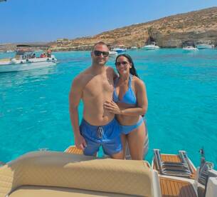 A couple poses happily on a boat in crystal-clear turquoise waters, capturing a perfect moment of joy and relaxation during their summer getaway.