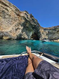 A person relaxes on the deck of a boat, enjoying the stunning turquoise waters and rocky cave formations — a perfect scene for a day of leisure on the water.