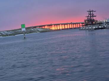 A stunning sunset casts vibrant colors over the harbor, featuring a pirate ship and a bridge in the background — a picturesque scene perfect for evening boat trips.