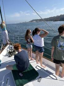 A group of friends and family enjoy a sailing trip, taking in the scenic views of the coastline while aboard a yacht.
