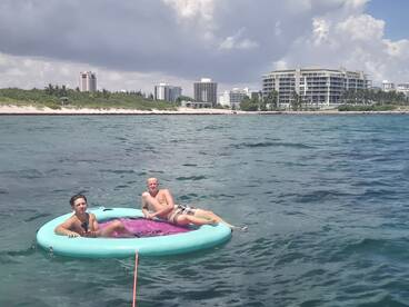 Two young men relax on a floating mat in the clear waters, enjoying a sunny day at the beach — a perfect scene for summer fun and water activities.