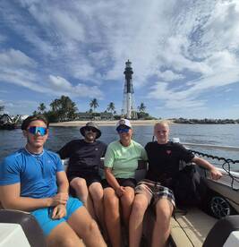 A cheerful group enjoys a day on the water, posing in front of a picturesque lighthouse — a perfect family outing under the sun.