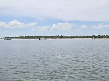 A picturesque view of boats anchored near a sandy coastline, with people enjoying the serene environment — perfect for island hopping adventures.