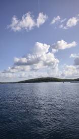 A scenic view of a calm water body with clouds overhead and a distant island, creating a tranquil atmosphere.