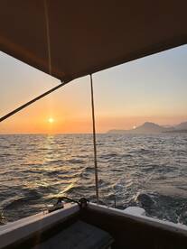 A serene sunset view from the deck of a boat, showcasing the tranquil ocean and distant mountains — perfect for romantic evening cruises.
