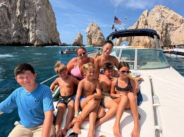 A joyful family poses together on a boat in Cabo San Lucas, surrounded by stunning rock formations — a perfect snapshot of a fun day on the water.