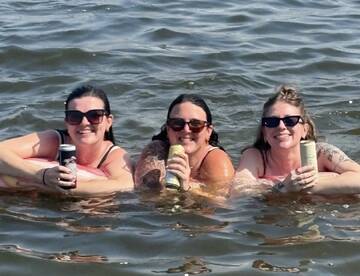 Three friends enjoy a fun day in the water, relaxing with drinks and floating on inflatable rings — perfect for summer parties and memorable outings.