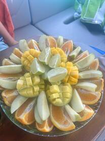 A vibrant fruit platter featuring a colorful assortment of mango, lime, apple, and orange slices, perfect for enjoying fresh snacks while on a boat trip.