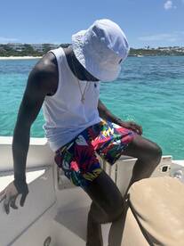 A man enjoys a sunny day on a boat, dressed in vibrant summer attire, with a beautiful beach backdrop — perfect for summer adventures on the water.