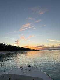 A serene sunset view from the bow of a boat, showcasing tranquil waters and a picturesque shoreline — perfect for evening cruises.