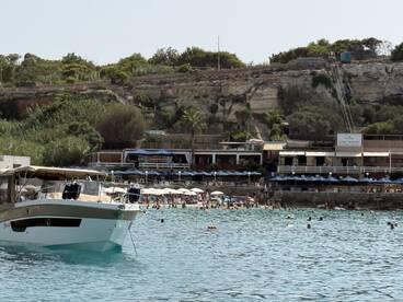 A scenic view of a boat anchored near a bustling beach, where guests enjoy swimming and sunbathing — a perfect summer getaway.