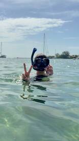 A child enjoys snorkeling in clear waters, flashing a peace sign while surrounded by a beautiful marine environment — a perfect moment for family adventures.