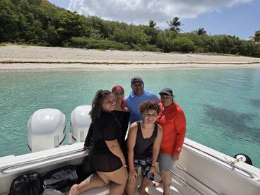 A cheerful group poses on the boat with a beautiful beach backdrop, capturing a memorable family outing in the sun.