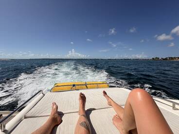 A couple relaxes on the deck of a boat, enjoying the sunny ocean view as they cruise through beautiful waters — a perfect moment for unwinding and soaking up the sun.