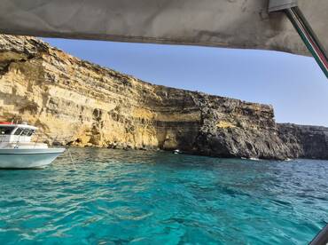 A stunning view of a boat anchored near a dramatic cliffside, showcasing the vibrant turquoise waters and rugged coastline — perfect for exploring scenic destinations.