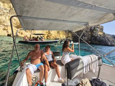 A family enjoys a sunny day on a boat, capturing the stunning scenery around them. The vibrant waters and rocky cliffs create a picturesque backdrop for their adventure.