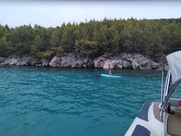 A paddleboarder glides across the turquoise waters near a rocky shoreline, showcasing the serene beauty of the coastal landscape.